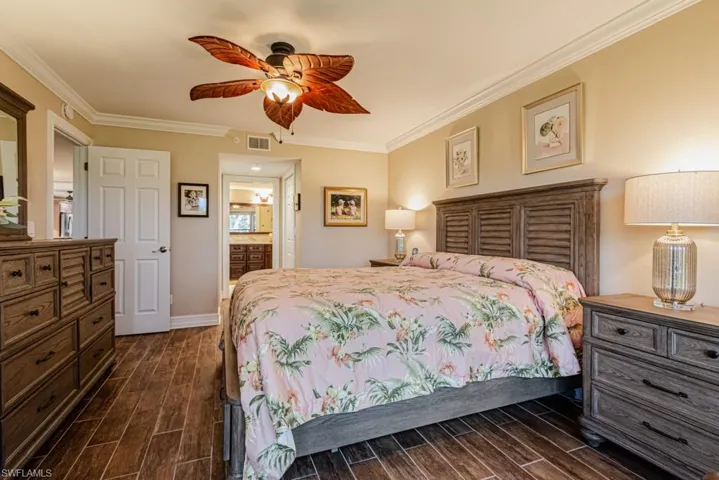 Bedroom with connected bathroom, ceiling fan, crown molding, and wood plank tile flooring.
