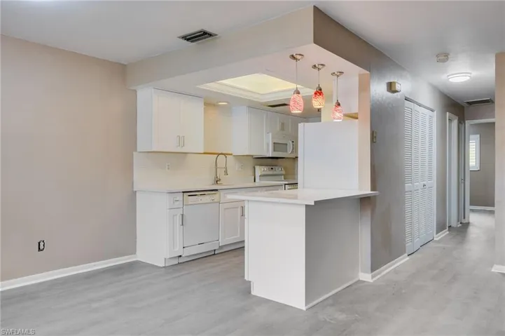 Kitchen featuring white cabinetry, white appliances, pendant lighting, light wood-style flooring, and a peninsula