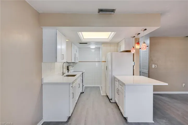 Kitchen featuring white cabinets, white appliances, light wood-type flooring, light stone countertops, and tile walls