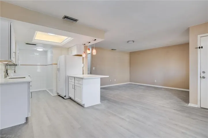 Kitchen featuring white cabinetry, light stone counters, open floor plan, freestanding refrigerator, and light wood-style floors