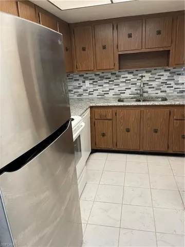 Kitchen with backsplash, sink, light tile flooring, and fridge