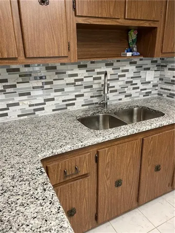 Kitchen featuring sink, light stone countertops, backsplash, and light tile floors