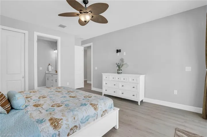 Bedroom with ensuite bathroom, with LVP wood-style flooring and ceiling fan