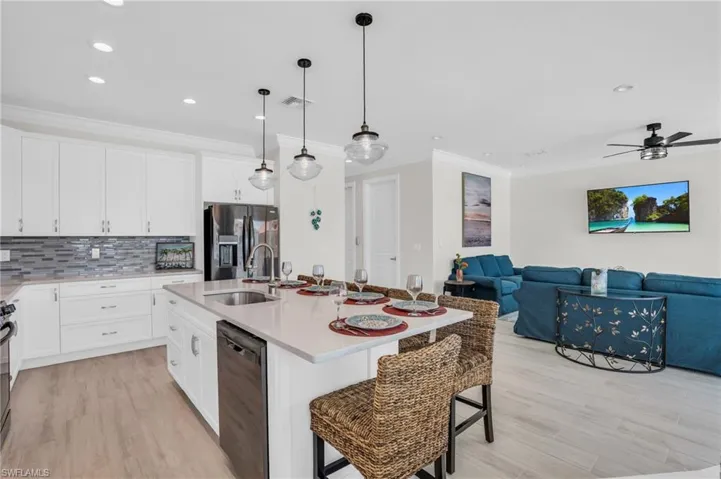 Kitchen with a kitchen bar, stainless steel appliances, backsplash, an island with sink, and ceiling fan