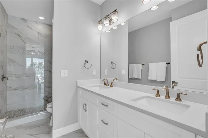 Bathroom featuring a shower with shower door, tile patterned flooring, toilet, and double sink vanity