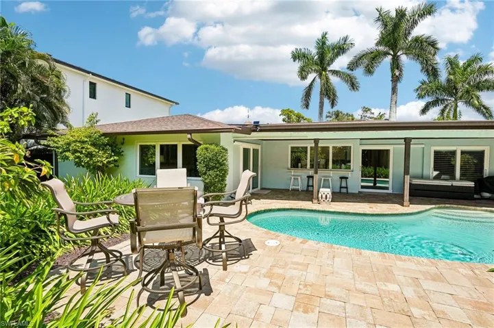 Freeform swimming pool with integrated steps, surrounded by paver decking, a covered patio, and lush landscaping