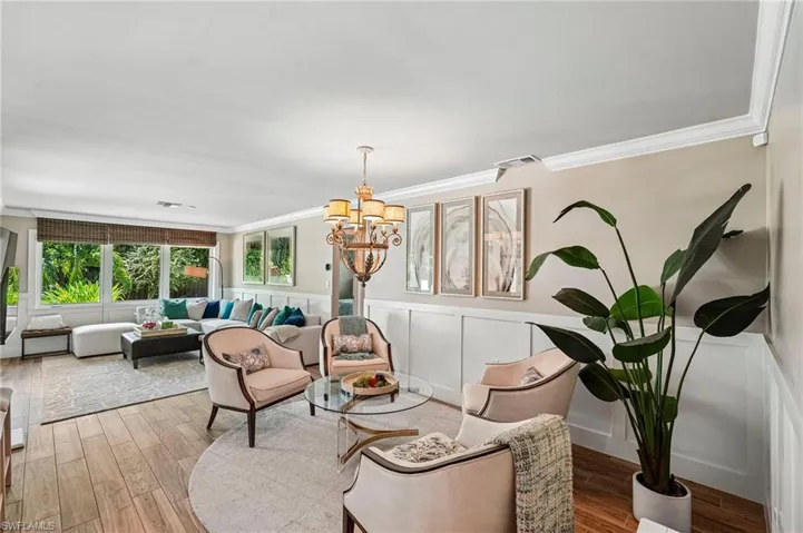 Spacious living area featuring wood-finish flooring, white wainscoting, crown molding, and large windows