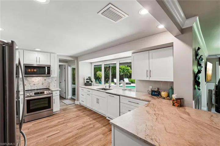 White cabinetry, stainless steel appliances, stone countertops, a decorative tile backsplash, and wood-finish flooring