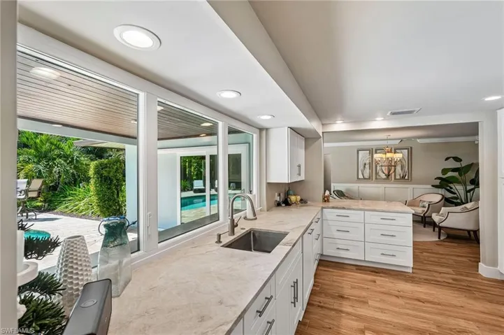 Kitchen featuring white cabinetry, stone countertops, stainless steel sink with a gooseneck faucet, and wood-finish flooring
