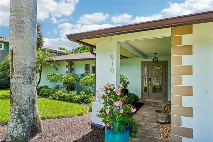Covered entry with decorative double doors, brick paver walkway, stucco exterior with stone accents, and mature landscaping