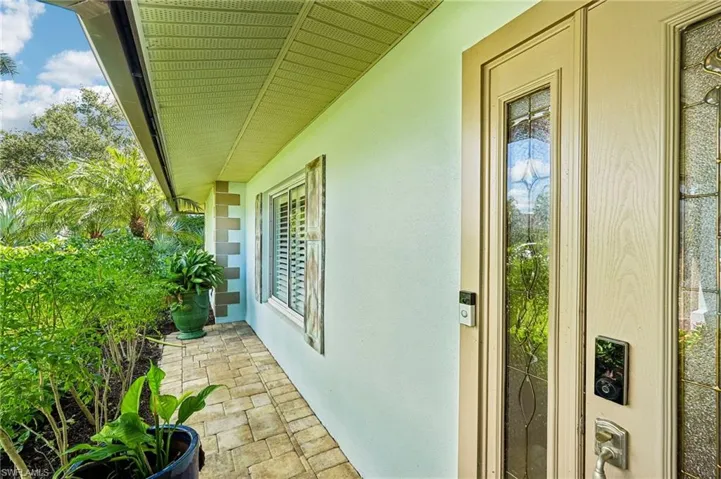 Entryway featuring a wood-finish door with decorative glass inserts, paver walkway, and lush landscaping
