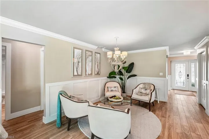 Crown molding, chair rail with wainscoting, wood-finish flooring, and a decorative chandelier