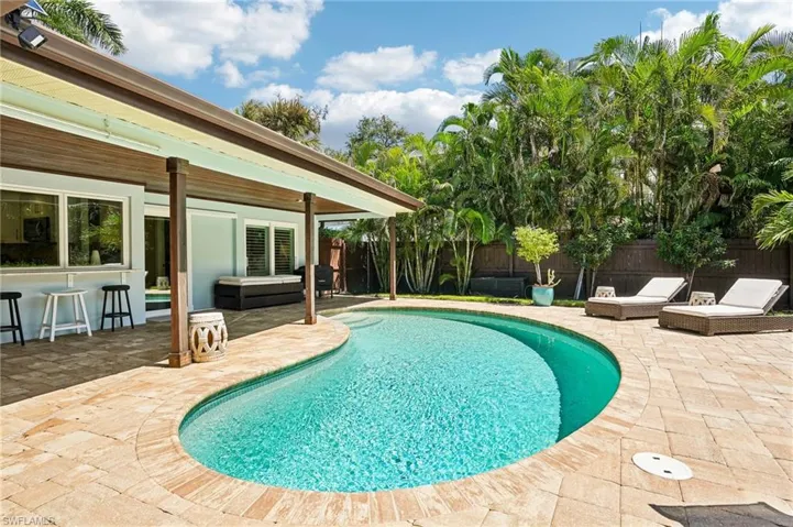 Freeform swimming pool, extensive paver patio, covered patio, lush tropical landscaping, and a privacy fence