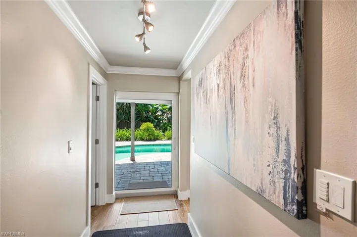 Recessed ceiling lights, crown molding, wood-finish flooring, and a sliding glass door opening to a paved patio and swimming pool
