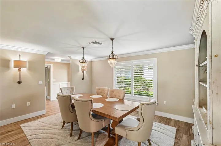 Wood-finish flooring, crown molding, double pendant light fixtures, wall sconce, and window with plantation shutters