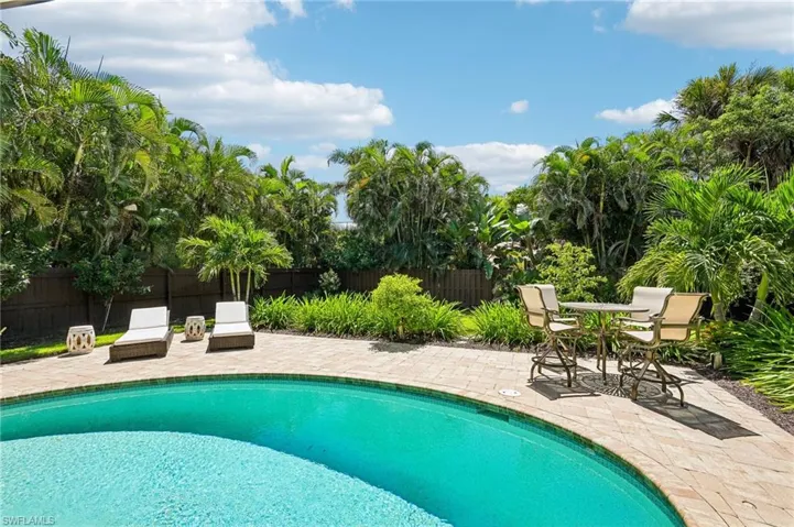 Outdoor swimming pool with a paver deck, surrounded by mature tropical landscaping and a privacy fence
