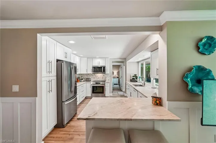 Kitchen featuring white cabinetry, stainless steel appliances, a stone countertop island, wood-finish flooring, and recessed lighting