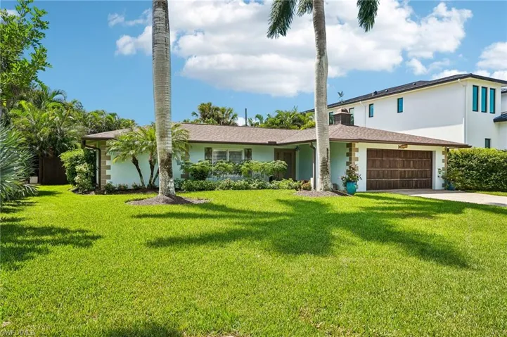 Expansive front lawn with mature palm trees, single-story residence with a pitched roof, and an attached garage with a wood-finish door