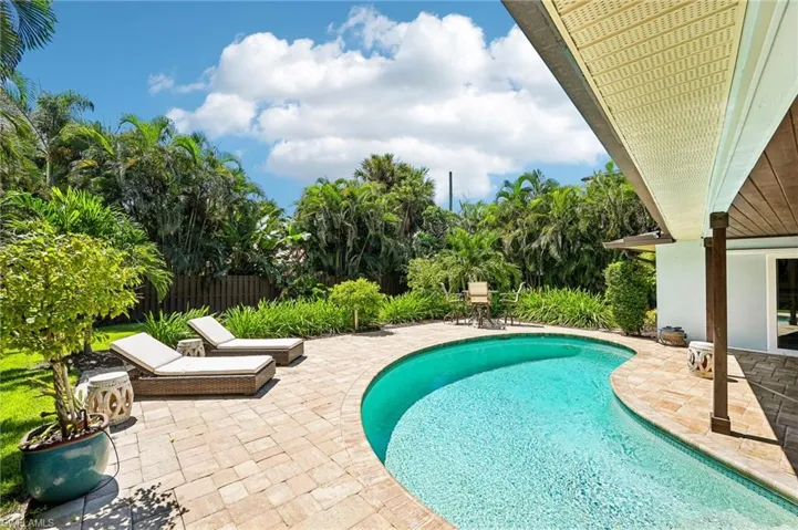 Curved swimming pool with mosaic tile accents, surrounded by a paver patio