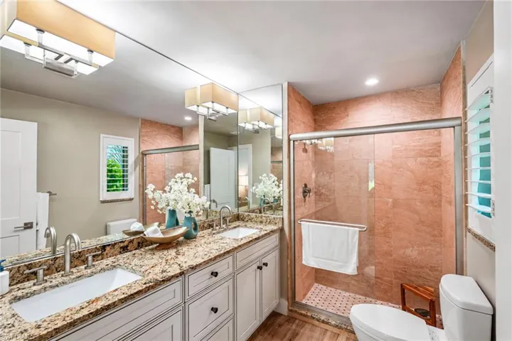 Dual vanity with granite countertop and undermount sinks, full-width mirror, and a glass-enclosed shower with tile surround