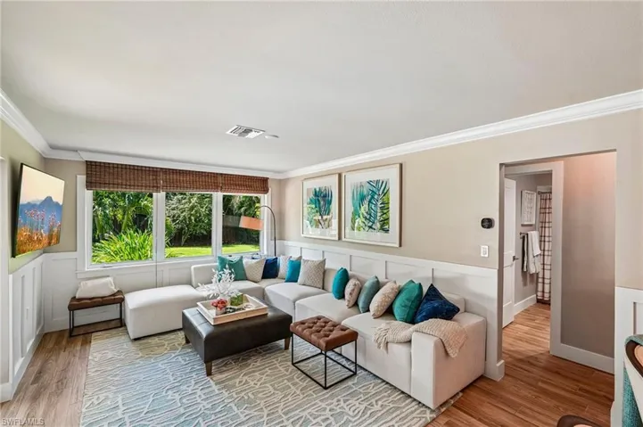 Wood-finish flooring, white wainscoting, crown molding, and large windows with natural woven shades