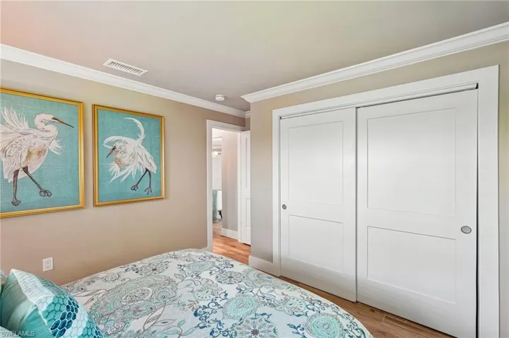 White crown molding, neutral wall color, white sliding closet doors, wood-finish flooring, and a white recessed ceiling fixture