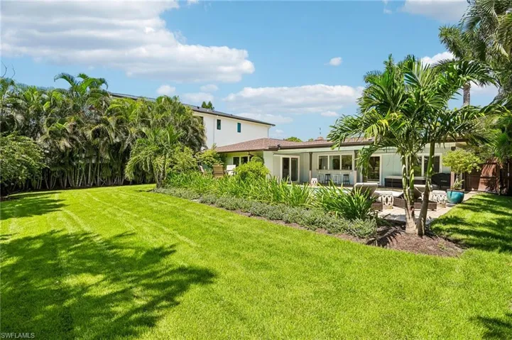 Expansive lawn area with mature landscaping, a paved patio, and multiple large windows across the rear elevation