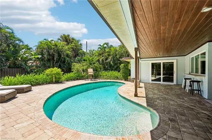 Freeform swimming pool with a paver surround, covered patio featuring a wood-finish ceiling, and built-in outdoor bar