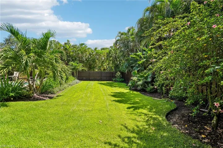 Expansive green lawn bordered by tropical landscaping, mature palm trees, and a privacy fence