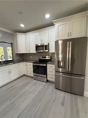 Kitchen with appliances with stainless steel finishes, white cabinets, dark stone counters, backsplash, and recessed lighting
