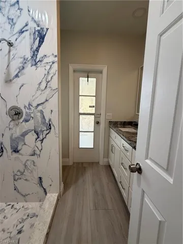 Full bathroom featuring vanity, a marble finish shower, and light wood-type flooring