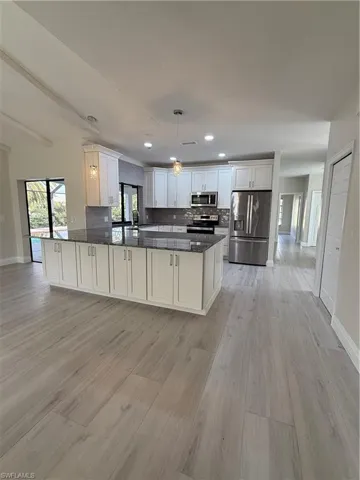Kitchen featuring refrigerator, white cabinets, decorative light fixtures, stainless steel range with gas cooktop, and dark stone countertops