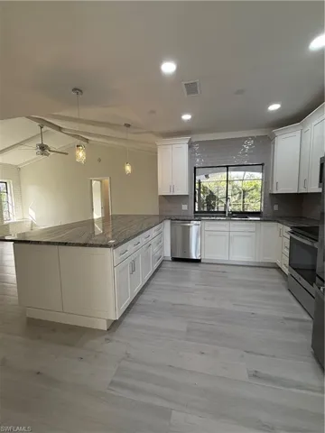 Kitchen with healthy amount of natural light, dark stone countertops, pendant lighting, white cabinets, and recessed lighting