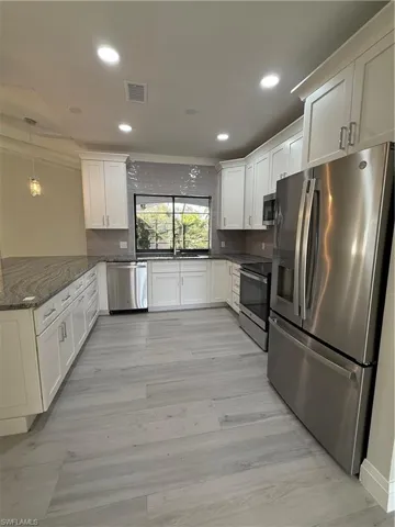 Kitchen featuring appliances with stainless steel finishes, white cabinetry, pendant lighting, dark stone countertops, and recessed lighting