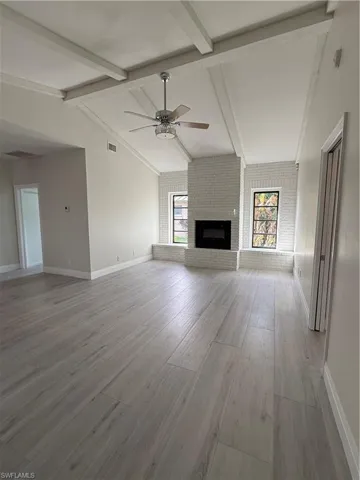 Unfurnished living room featuring brick wall, a fireplace, a ceiling fan, and light wood-type flooring