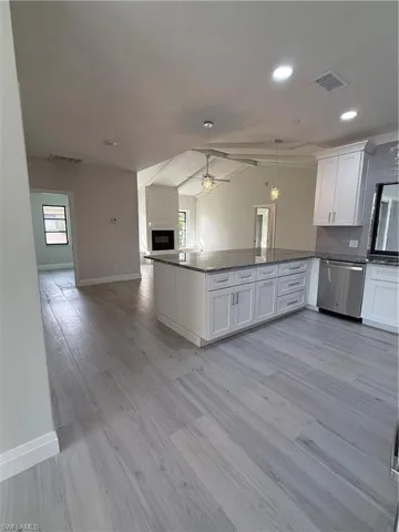 Kitchen with open floor plan, vaulted ceiling, white cabinets, decorative light fixtures, and dishwashing machine