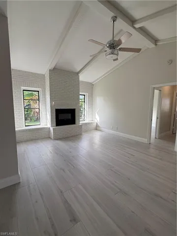 Unfurnished living room with brick wall, a fireplace, light wood-type flooring, and ceiling fan