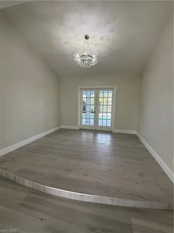 Empty room with french doors, a chandelier, and light wood finished floors