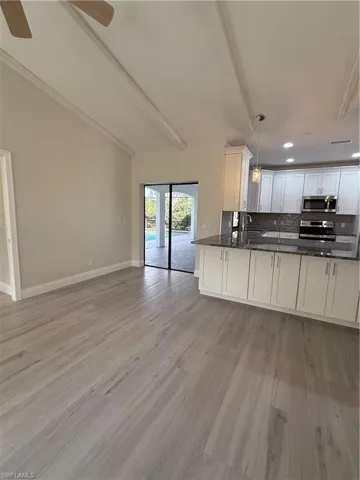 Kitchen featuring open floor plan, decorative light fixtures, stove, white cabinetry, and dark stone countertops