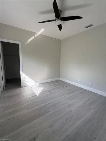 Unfurnished bedroom with a spacious closet, ceiling fan, and light wood-type flooring
