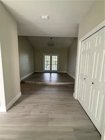 Unfurnished dining area featuring a chandelier, light wood-style floors, vaulted ceiling, and french doors