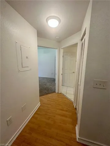 Corridor featuring baseboards a textured wall, and light wood-style floors