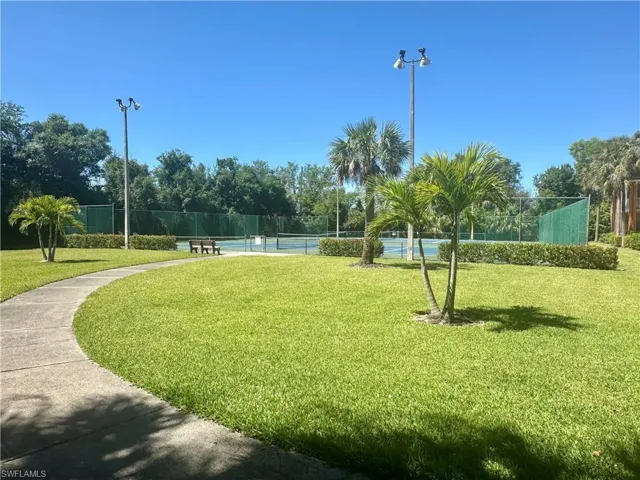 Surrounding community with a lawn, fence, and a tennis court