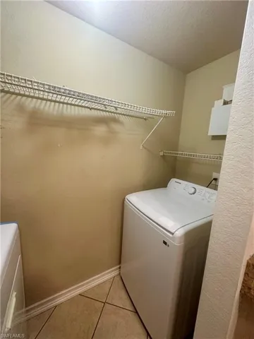 Washroom featuring washing machine and clothes dryer, a textured ceiling, baseboards, laundry area, and light tile patterned floors