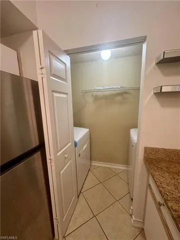 Washroom with washer and clothes dryer, laundry area, baseboards, and light tile patterned floors