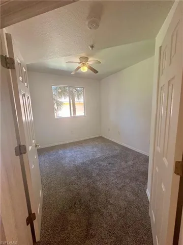 Unfurnished room with a textured ceiling, baseboards, ceiling fan, and dark carpet
