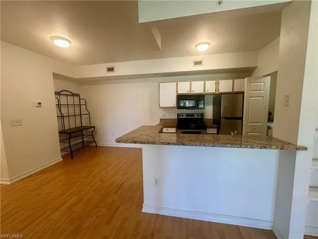Kitchen featuring white cabinets, a peninsula, baseboards, appliances with stainless steel finishes, and light wood-style floors