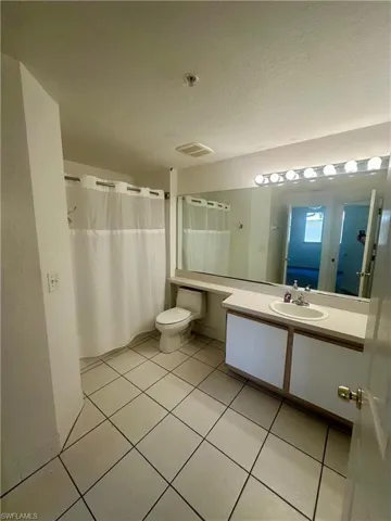 Bathroom with tile patterned floors, toilet, curtained shower, vanity, and a textured ceiling
