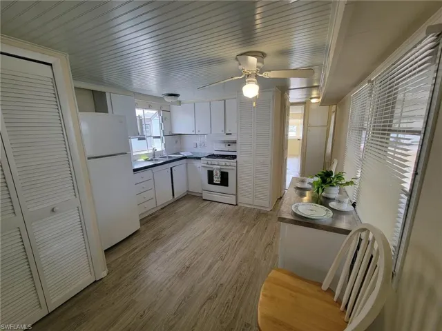 Kitchen featuring white cabinets, white appliances, tasteful backsplash, dark countertops, and light wood-style flooring