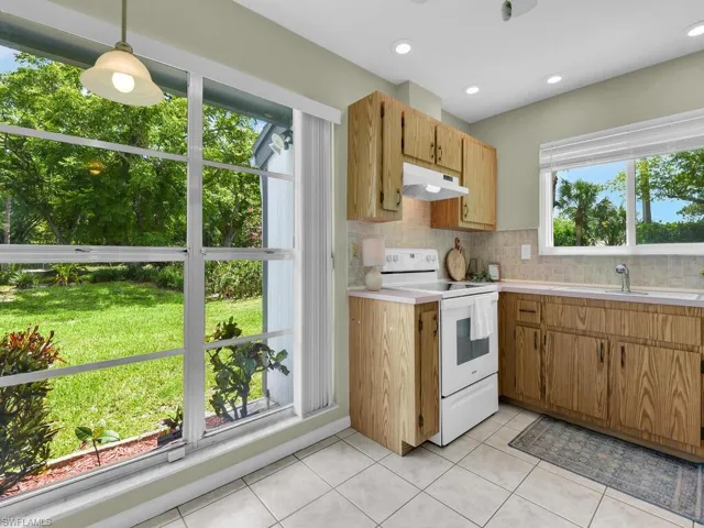 Kitchen featuring white electric range, light countertops, under cabinet range hood, tasteful backsplash, and light tile patterned floors